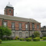 Image of a Dundee University part red part grey brick building with some trimmed decorative hedges in front